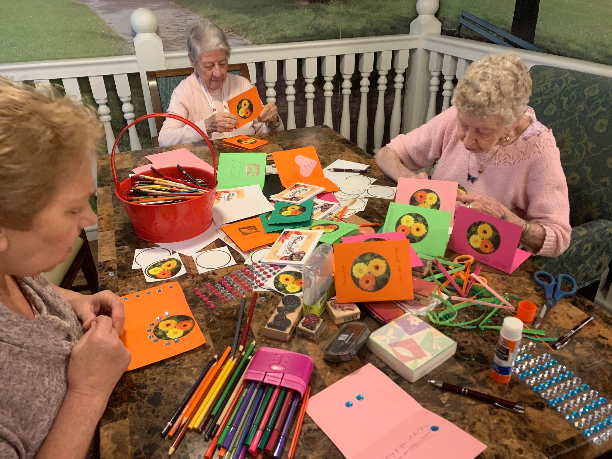 Group of senior women sitting at a table making cards with coloured pencils paper and sequins