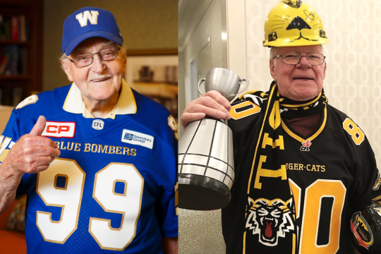 two senior men in football jerseys holding a grey cup and football