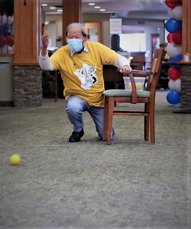 Asian senior man in mask kneeling and throwing a ball