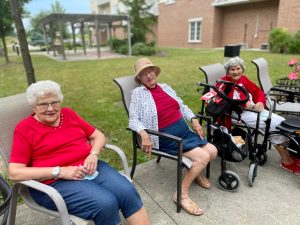 Three senior women in red shirts sitting in the sun.