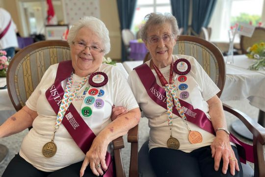 Two older women with grey hair wearing Seniors Games T-shirts sporting medals