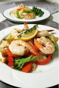 Shrimp and vegetables on a white plate topped with slice of lemon