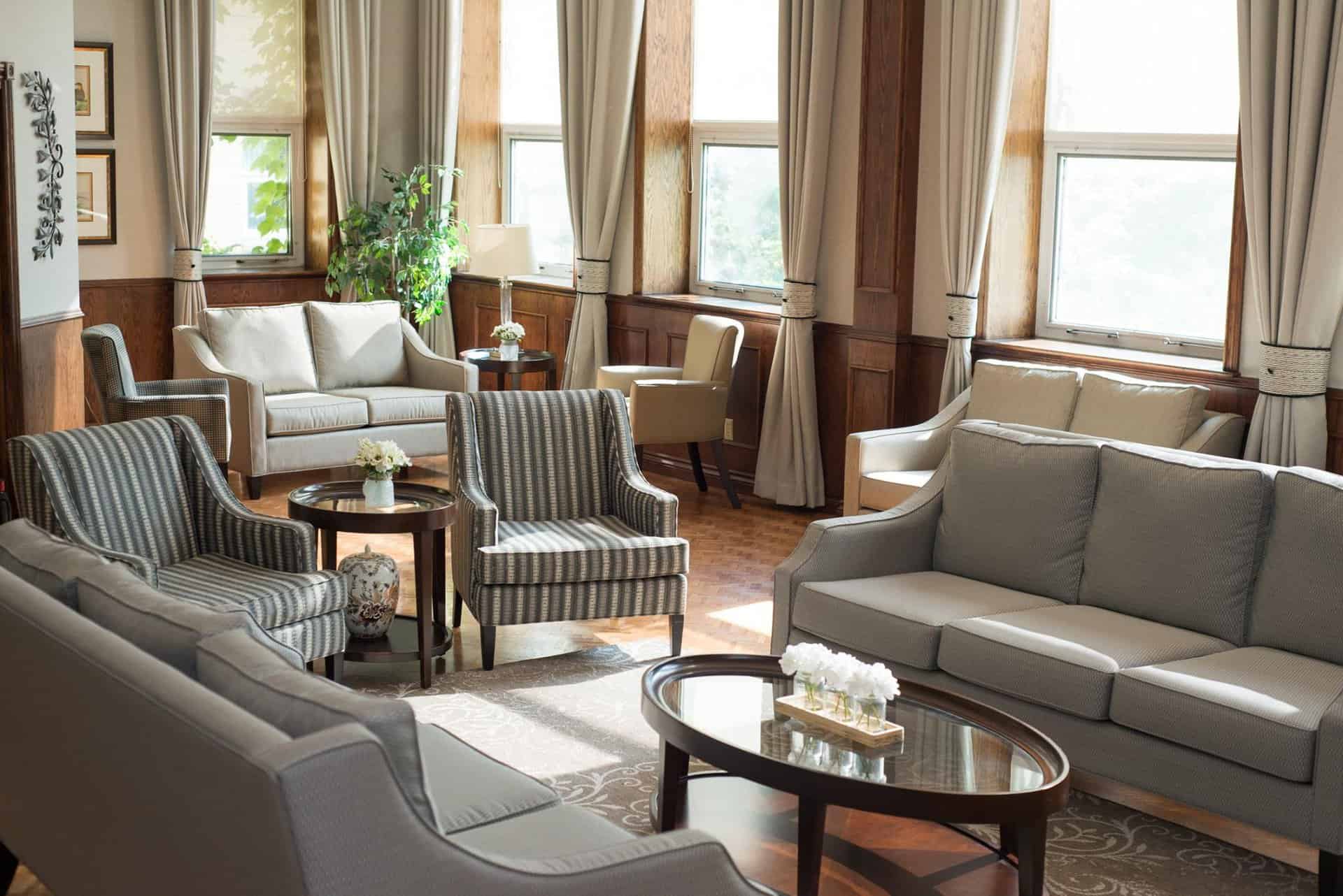 Le guide ultime pour déménager dans une communauté de retraités (et une liste de contrôle) - All Seniors Care Sun filled living area with grey couches and glass coffee table.