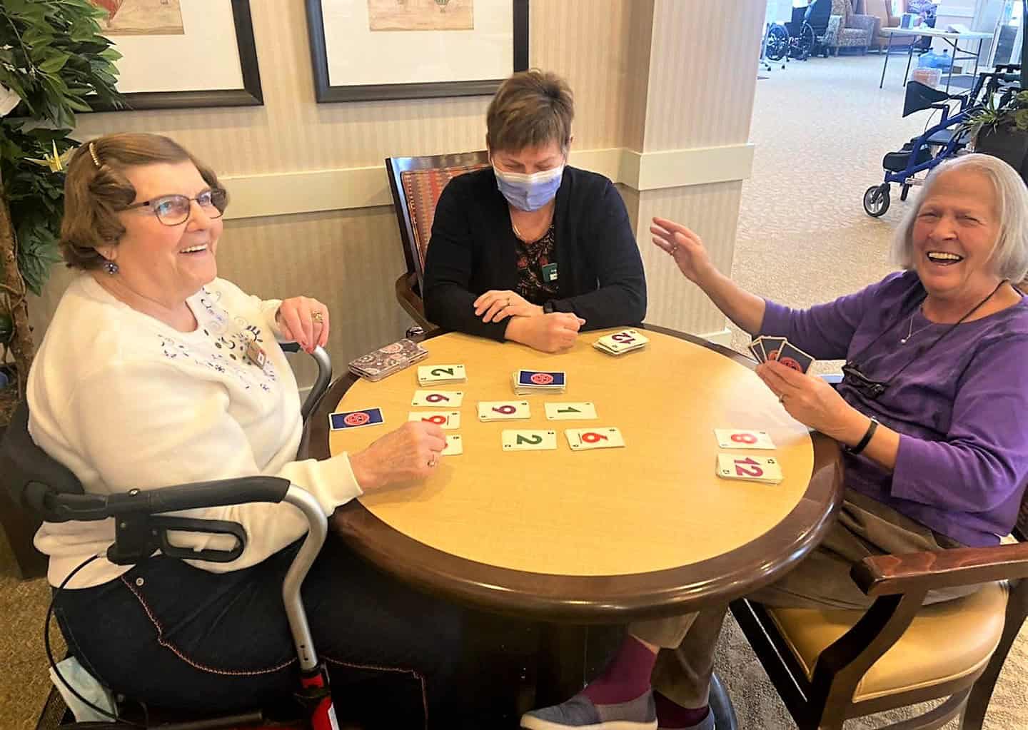 In The Spotlight: The Recreation Therapy A-Team - All Seniors Care Three senior women sitting at a round table, playing Uno, and laughing.