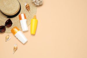 Beach accessories with sunscreen cream on color background