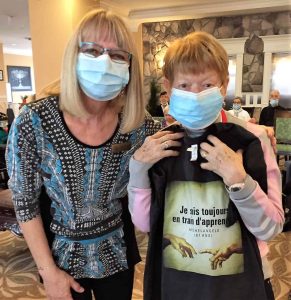 Deux femmes portant des masques, l'une tenant un t-shirt d'événement infiniment curieux.