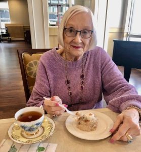 Conseils pour les soins de la peau des personnes âgées l’hiver - All Seniors Care Youthful 90 year old woman with long hair and glasses, pink sweather, having high tea.