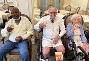 Three older adults sitting, multicultural, cheers, eating popcorn