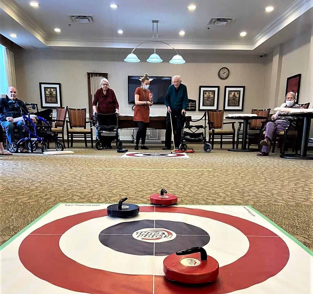 In The Spotlight: The Recreation Therapy A-Team - All Seniors Care Modified curling game; seniors in the background using shuffleboard cue to push the rocks.