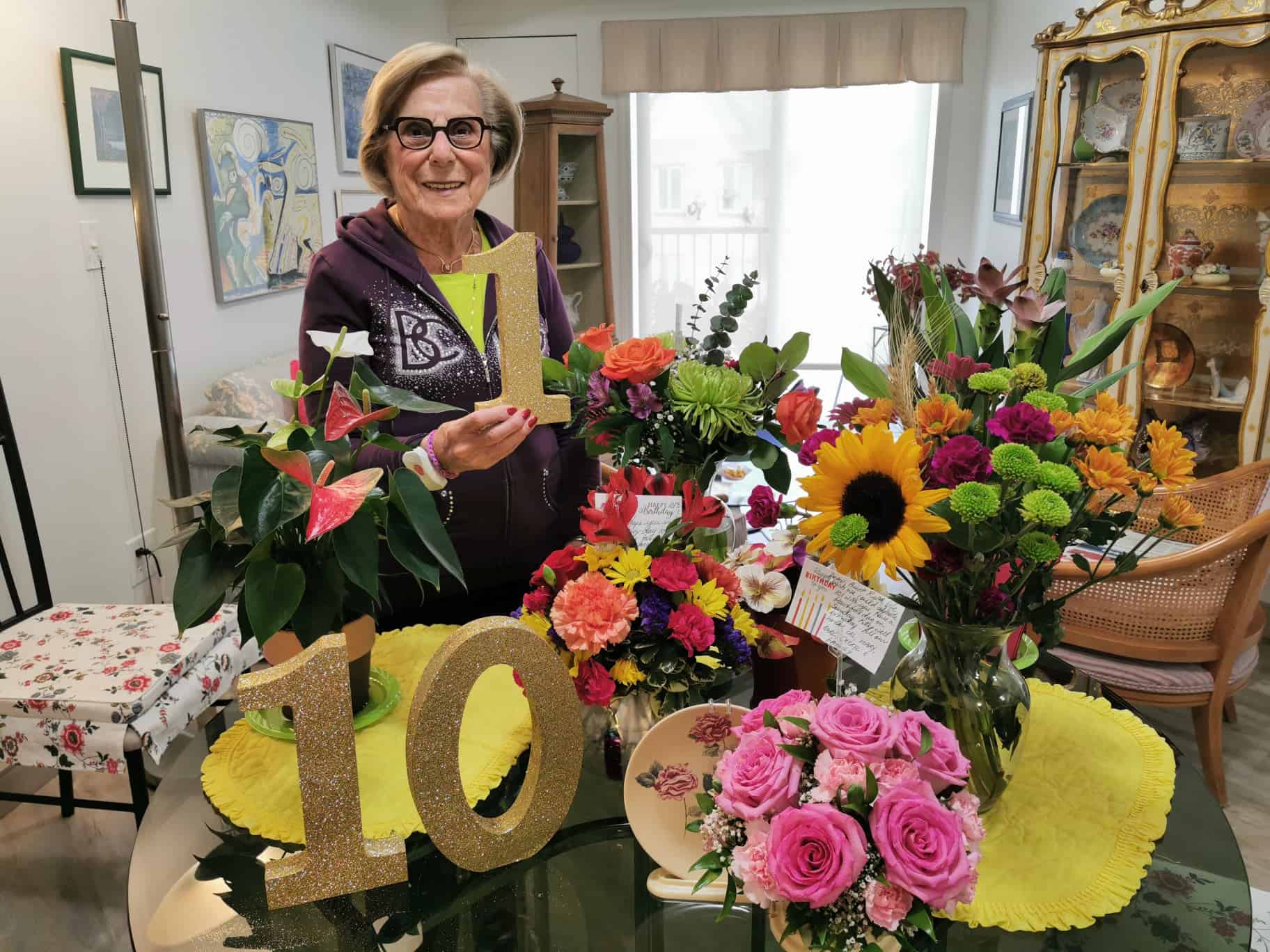 Senior woman with glasses celebrating her 101 birthday with flowers in her retirement suite